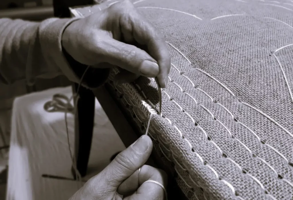 Mains de Béatrice Gouin, artisan tapissier réalisant un piquage sur garniture d'un fauteuil en cours de restauration.